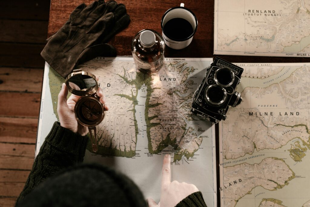 Top view of vintage exploration setup with maps, compass, gloves, and retro camera.